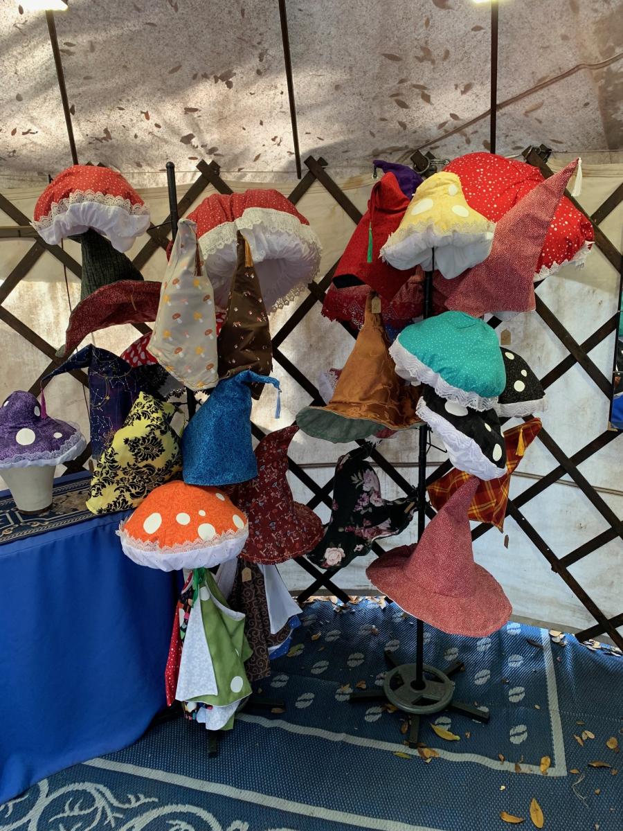 A crowded stand of artisan hats inside the yurt, including mushroom hats and pointed wizard hats against wooden lattice.