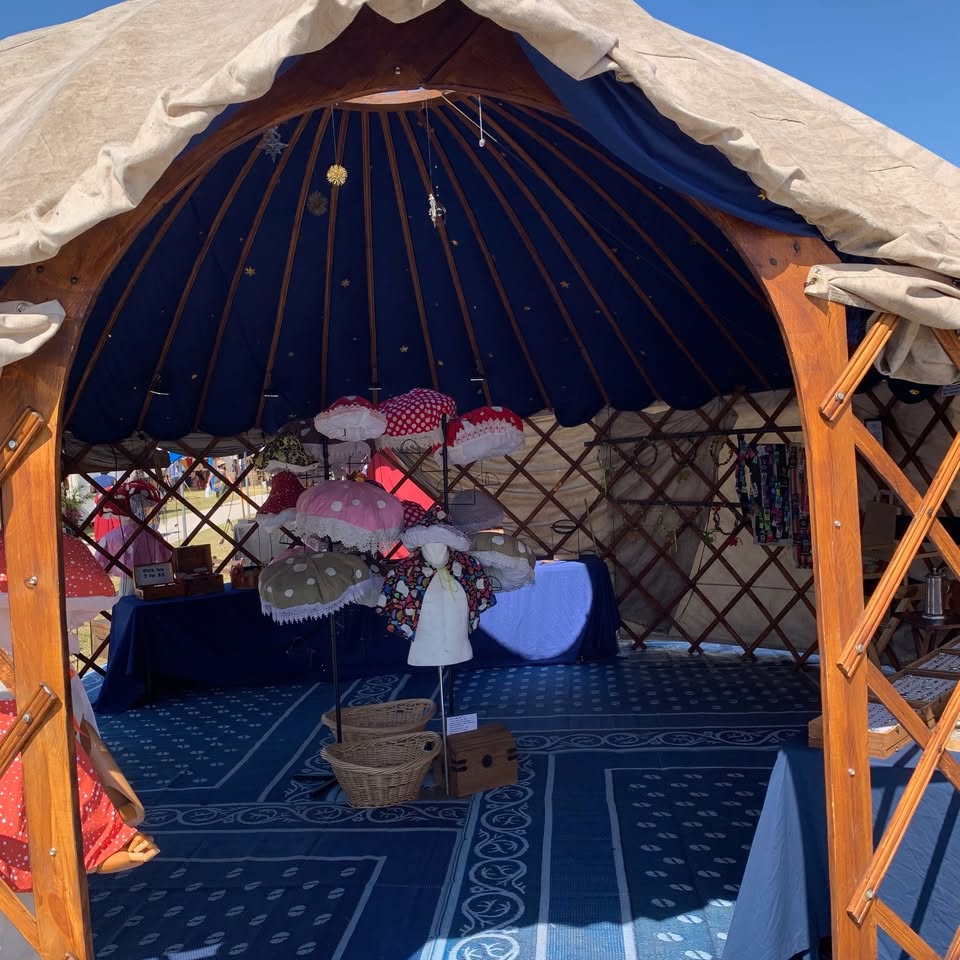 Looking through the arched doorway of the Treasure Yurt: wooden lattice walls, a deep royal-blue ceiling scattered with gold stars, and a stand of mushroom hats.