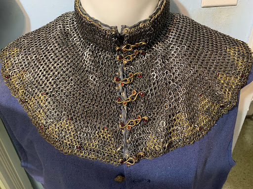 Jeweled decorative maille collar of silver and gold rings with small red stones, displayed on a mannequin over a navy garment.